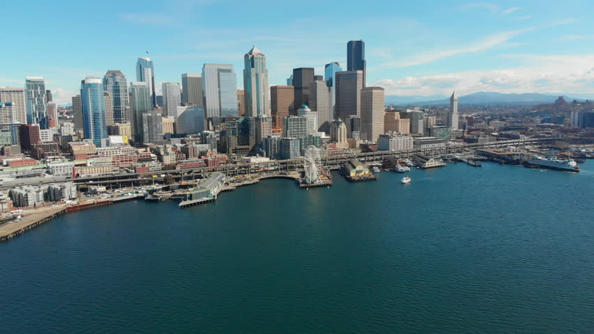 Aerial Shot Flying in From the Water to the Waterfront and Downtown Skyscrapers in Seattle, Washington with Freeway, Buses, Pedestrians, and an Aquarium in View.