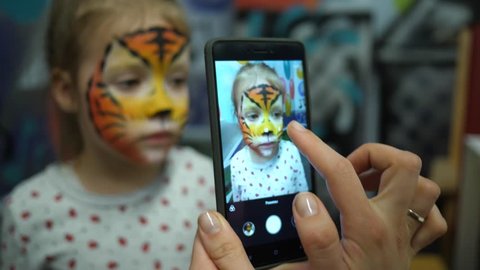 Body art painted face cute little girl on birthday theme party taking phone picture for instagram