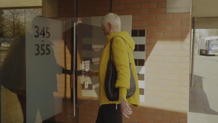Happy woman using intercom at building entrance 
