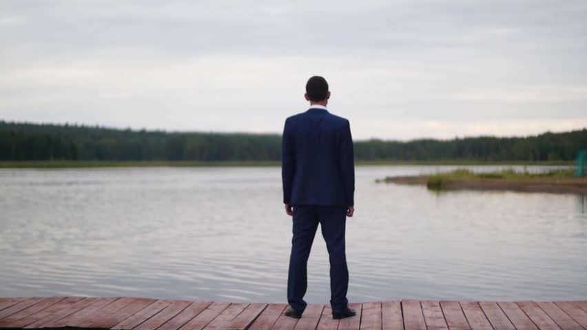Businessman looking at the lake. Clip. Rear view of businessman looking at picturesque nature landscape. Businessman stand on berth