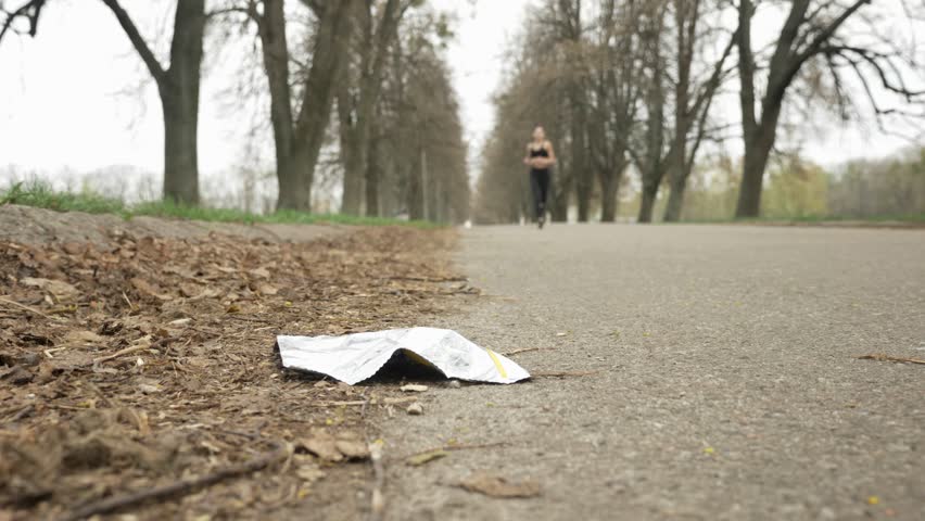 Young beautiful girl in a black sport suit running on the road in a blooming park, bottom view, plogging concept, 50 fps