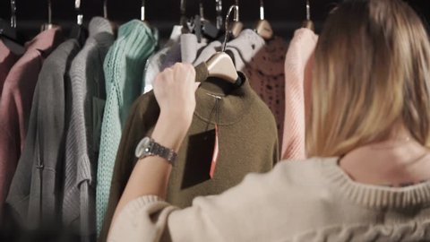 a young woman holds a warm sweater on her hanger, on which a tag with a price weighs, a lady looks at the material from which this clothing is made