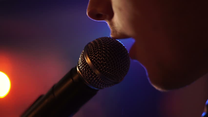 Man singing song in microphone during performance on stage on rock concert. Close up man rock star singer on music concert on colorful light background
