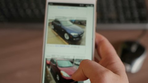 A man chooses to buy a car on the site. Looking at used vehicle to buy on a smartphone app. Close Up. Screen is blurred. 4K UHD. 