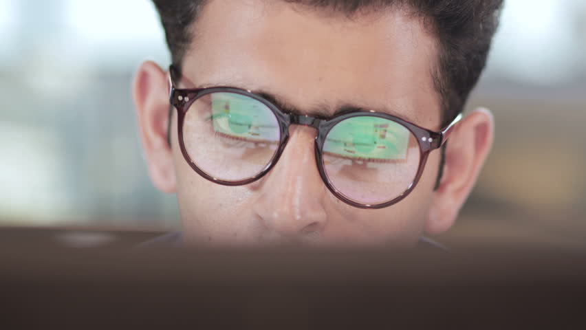 close up of a young and busy businessman wearing eyeglasses working on computer. Reflection of computer screen can be seen in the eyeglasses of an handsome male entrepreneur in modern corporate office Royalty-Free Stock Footage #1009955333