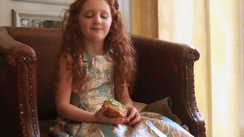 A cute redhead girl siting in a vintage chair with a donut