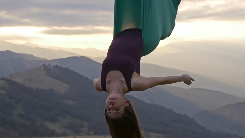 Woman in hammock meditating upside down at sunset. Anti-gravity yoga in the mountains