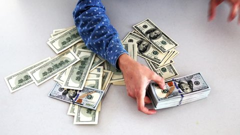 Dollar bills, money background. Hands flipping through a stack of US dollar bills with a large stack of hundred US dollar bills on background.