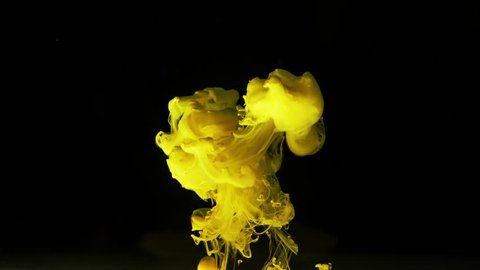 Colored yellow thick mass spreads upwards in the water on black background. Clubs of yellow thick smoke rise up. Yellow magic abstraction on black background. Slow motion.