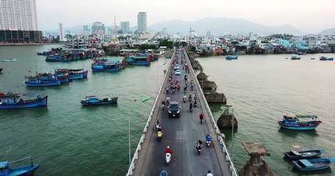 AERIAL 4K: Motorcycle and car traffic in Nha Trang Bridge, Vietnam. Boats near the bridge. CIty buildings in the background