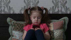 A cute little girl is playing with a smartphone, watching a video in the phone. Children and gadgets.