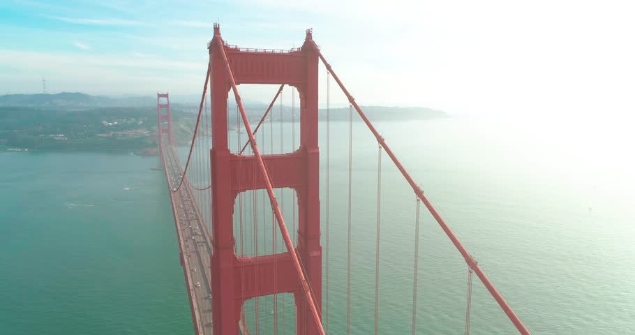 Aerial view of the Golden Gate landmark with San Francisco green hills on a background. Drone flight outbound the tower of the red bridge with the sunset view above the Pacific Ocean, West coast. 4K Royalty-Free Stock Footage #1009987178