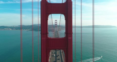Aerial video of the Golden Gate Bridge. Inspirational drone flight through the window of the red tower above the busy road. San Francisco downtown on the background at sunset. California, USA. 4K