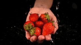 Strawberry in hands with water drop on black background. Front view. Slowmotion