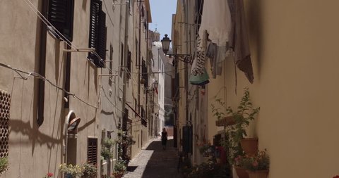 ALGHERO, SARDINIA, ITALY – JULY 2016 : Video shot of beautiful blonde girl walking in narrow street in central Alghero on a sunny day