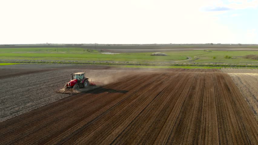 Tractor pulling land cultivating machine for sowing preparation. Sunny spring day. 4K aerial footage.