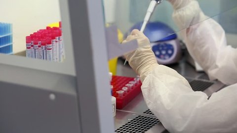 Young female scientist working in sterile genetics laboratory with pipette in white medical dressing gown and doctor cap.
