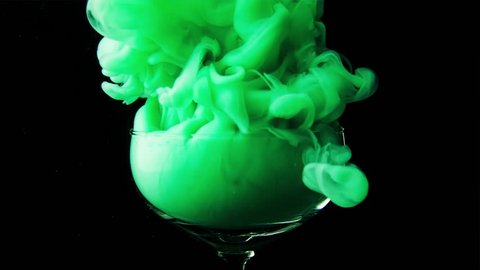 Beautiful glass goblet envelops thick green smoke. A magical and magical potion is poured into a glass vessel on a black background. Slow motion.
