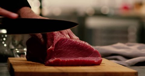 The chef cuts raw meat with the knife in Slow Motion