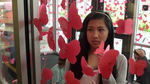 Asian girl decorating a glass wall with butterfly cutouts