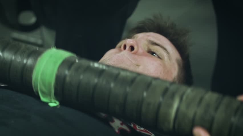 Young attractive man completes a rep of a bench press set and then gets up from the bench