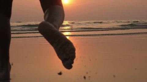 Silhouette of happy child running into sea in beautiful sunset light. Baby rushing toward water at sandy beach, rear view, slow motionの動画素材