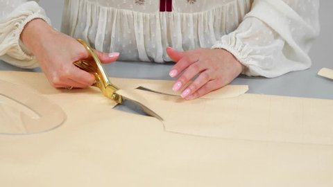 Young female designer with tape-line on her neck standing in dressmaking studio and drawing lines with chalk and rule. Female couturier in atelier cutting out a pattern for future clothes.
