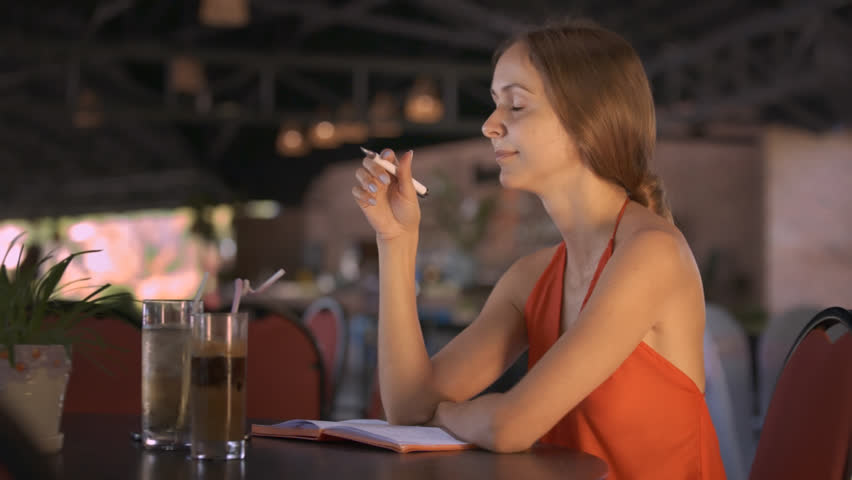 Closeup nice girl in red clothes recalled thought and writes down in diary sitting at table near beverages in cafe | Shutterstock HD Video #1010039516