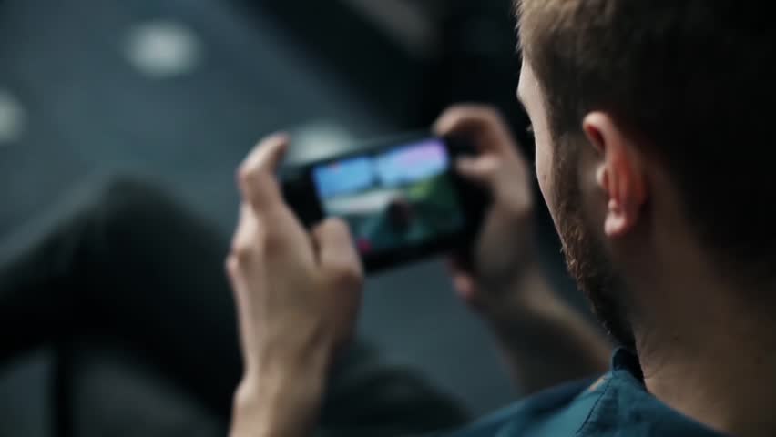 Young man with a beard casually playing Portable Video Game Console. Closeup.