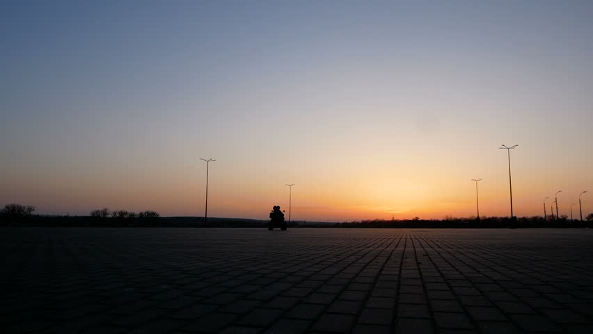 Young couple is riding a quad bike around a large square in the background of a beautiful sunset.