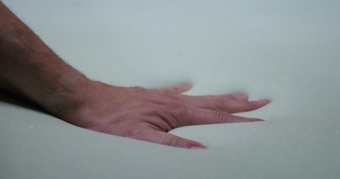 A hand slowly presses into a soft foam mattress.  	
