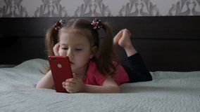A cute little girl is playing with a smartphone, watching a video in the phone. Children and gadgets.