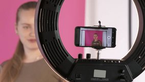 Teen girl vlogger recording video blog for her lifestyle channel in home vlog studio. Teenage blogger using smartphone mounted on LED ring light panel and portable background support system with paper