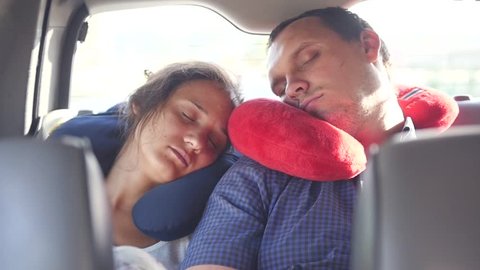 A pair of travelers, a man and a woman are sleeping in a car with special pillows on their necks, leaning against each other. slow motion. 1920x1080. full hd