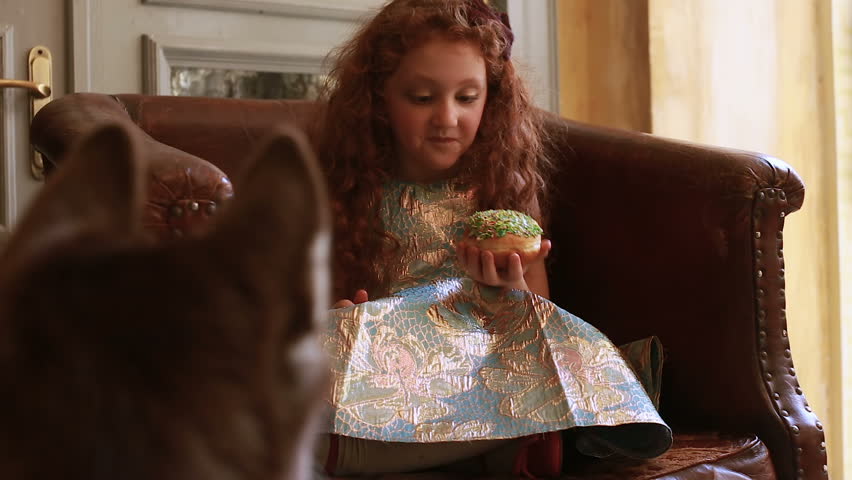 A cute redhead girl siting in a vintage chair with a donut
