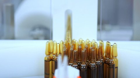 Pharmaceutical manufacturing at pharmacy factory. Close up of yellow medical ampoules on conveyor line. Medicine packaging line. Medicine bottles at automated production line