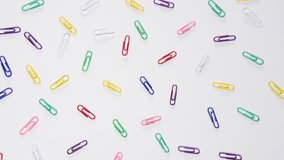 slow motion of coloured paper clips falling onto a white background, office and school work stationary, close up, macro shot.