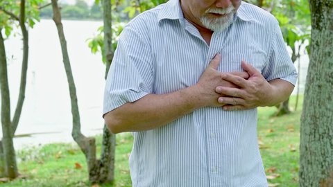 Senior man having a heart attack. Chinese old man is having chest pain. Outdoor in park.