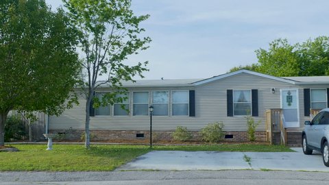 Establishing shot of a manufactured home with an SUV car in the driveway and a couple of trees with green leaves during the day - dolly shot