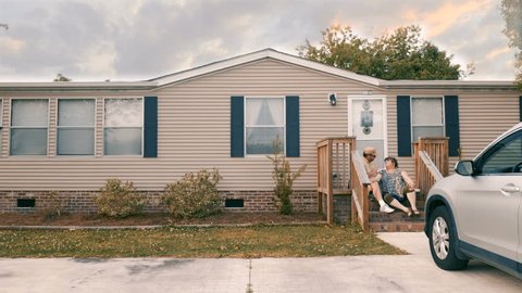 Man and woman couple sitting on porch steps of their manufactured home high five each other - wide dolly shot
