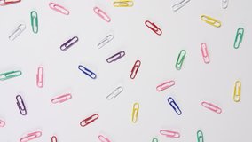 4k of coloured paper clips scattered onto a white background, individual bright office, school and work fun colour stationary cupboard supplies, a dolly shot over the top looking down. 