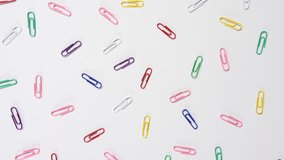 4k of coloured paper clips scattered onto a white background, individual bright office, school and work fun colour stationary cupboard supplies, a dolly shot over the top looking down. 