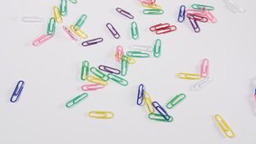 4k of bright coloured paper clips scattered onto a white background, individual bright office and work fun colour stationary cupboard supplies, a dolly shot from above looking down. 