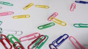 4k of coloured bright paper clips on a white background, individual office, school and work fun colour stationary paperclip supplies, dolly shot from above. 