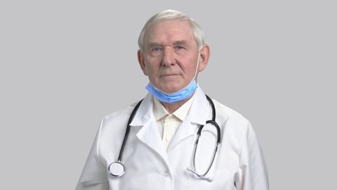 Wearing mask in grey isolated background. Elder doctor man put on wear medical mask in grey isolated background.