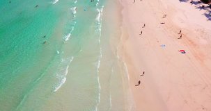 AERIAL 4K; Fly cam move along the sand beach overhead  of people enjoying the summer, sea waves breaking against the coast line