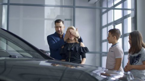 The successful husband made a gift to his wife and gave her a car, the woman is very emotional and surprised and they hug themselves together near the car.