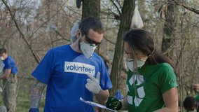 Tattooed man in t-shirt of volunteer and respirator talking to Asian girl coordinator about work process in cleanup. - Powered by Shutterstock - Get 15% off with code: PIKWIZARD15