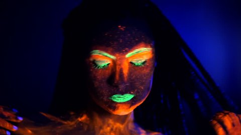 Fashion sexy dancer with braids in neon light. Fluorescent makeup glowing under ultraviolet light. Night club, party, halloween psychedelic concepts. Mysterious woman with UV painting