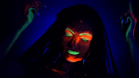 Fashion model woman with braids dancing in neon light. Fluorescent makeup glowing under UV black light. Night club, party, halloween psychedelic concepts.